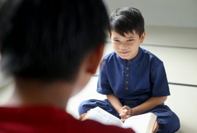 Rear view of Asian Muslim boy teaching brother how to read Quran inside the mosque