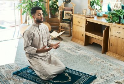 Shot of a young muslim man praying in the lounge at home
